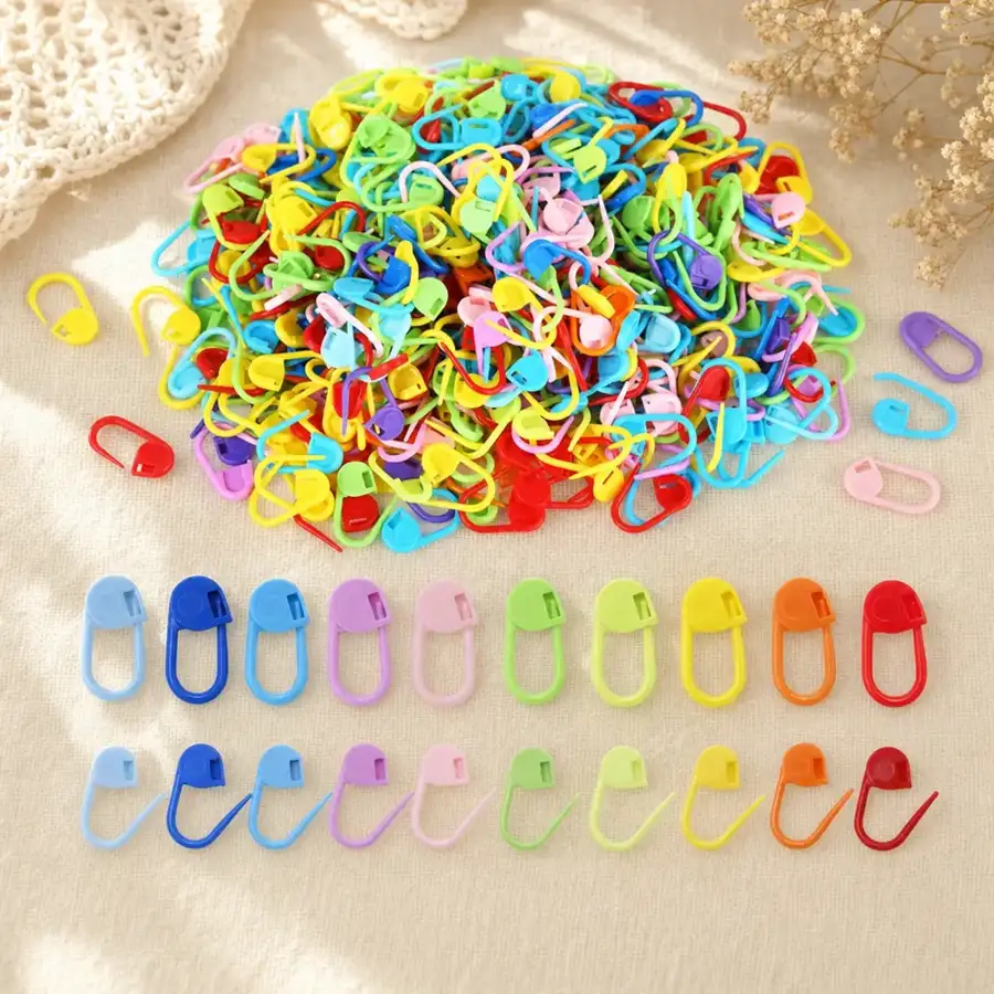 Flat lay of the Purlclip 50-pack: pile of assorted color locking stitch markers on warm linen